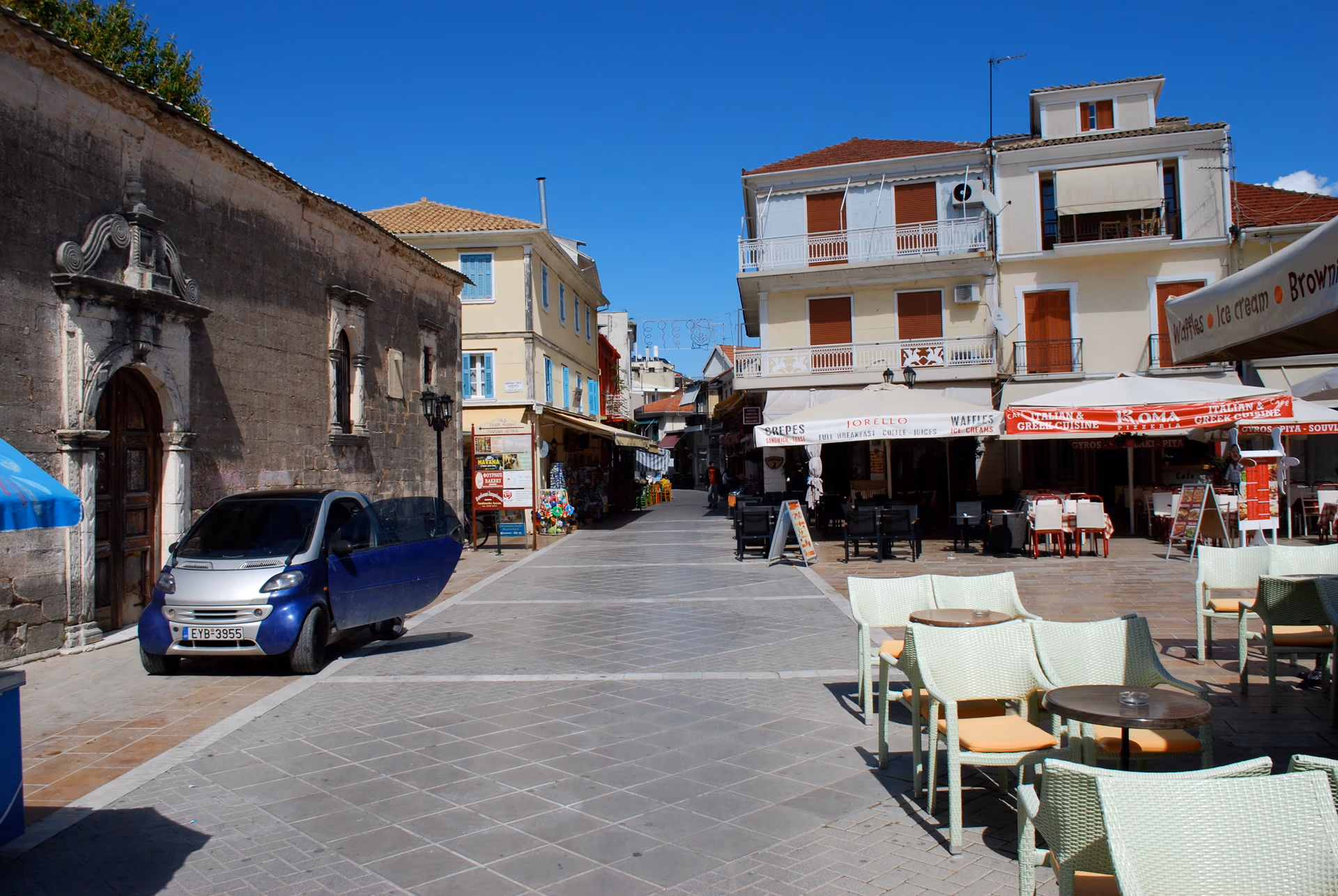 A paved square and pedestrian street in central Lefkada, with the stone church of Agios Spyridon to the left and buildings around it.