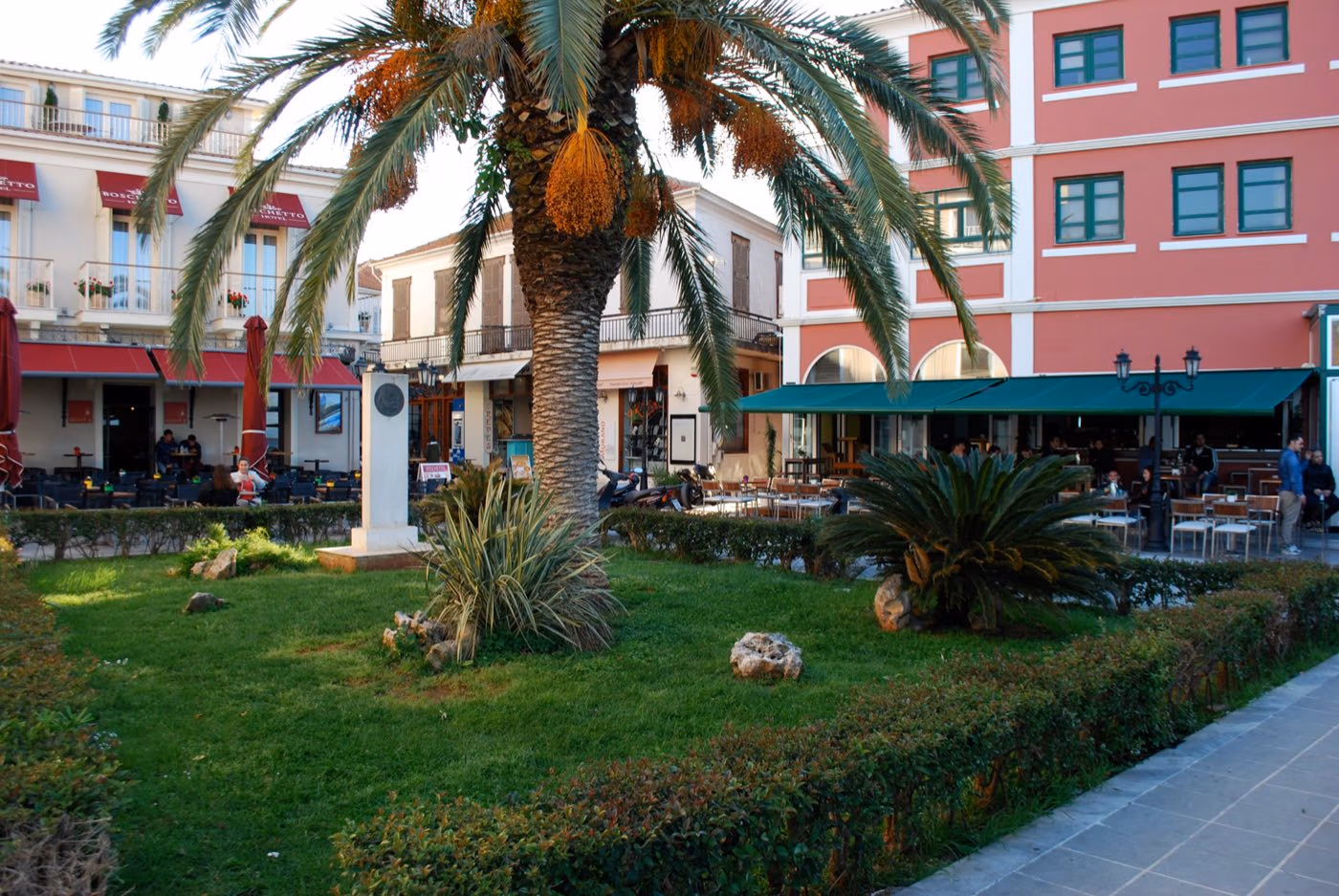A small memorial to Antonis Tzevelekis stands beside a palm tree in a square in Lefkada Town.