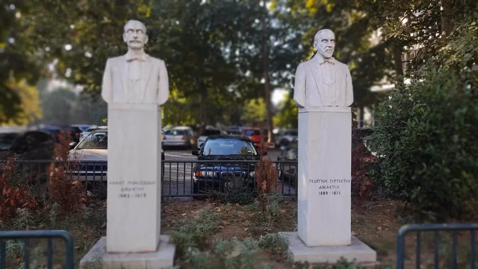 Two white marble busts of judges Anastasios Polyzoidis and Georgios Tertsetis in a garden; Tertsetis is in focus at right.
