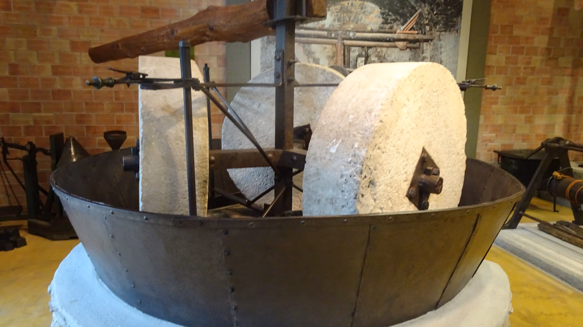A large stone millstone set upright in a round metal basin, part of a restored olive oil mill in a museum.