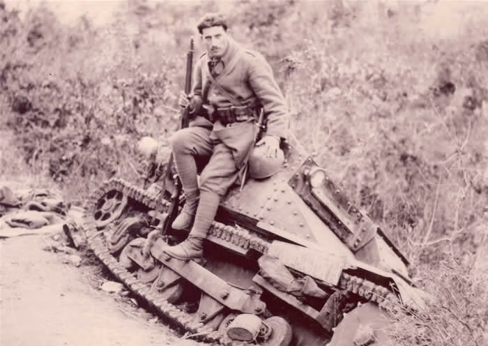 Soldier seated on a small tracked armoured vehicle tilted in a ditch
