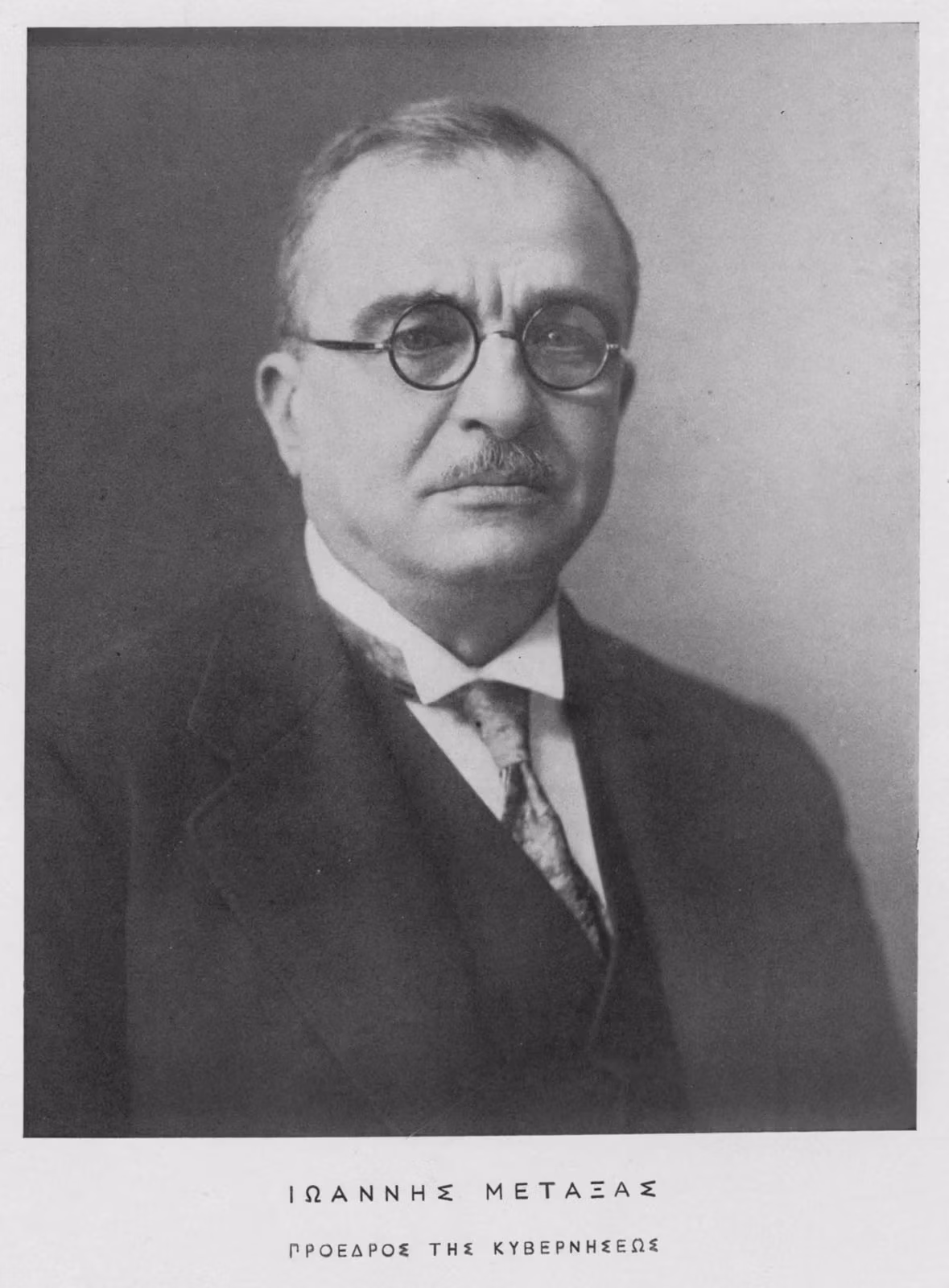 Studio portrait of an older man in round glasses, dark suit and tie