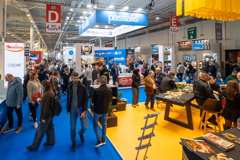 Visitors walk along a blue-carpeted FOOD EXPO aisle beside exhibition stands and a yellow seating area.