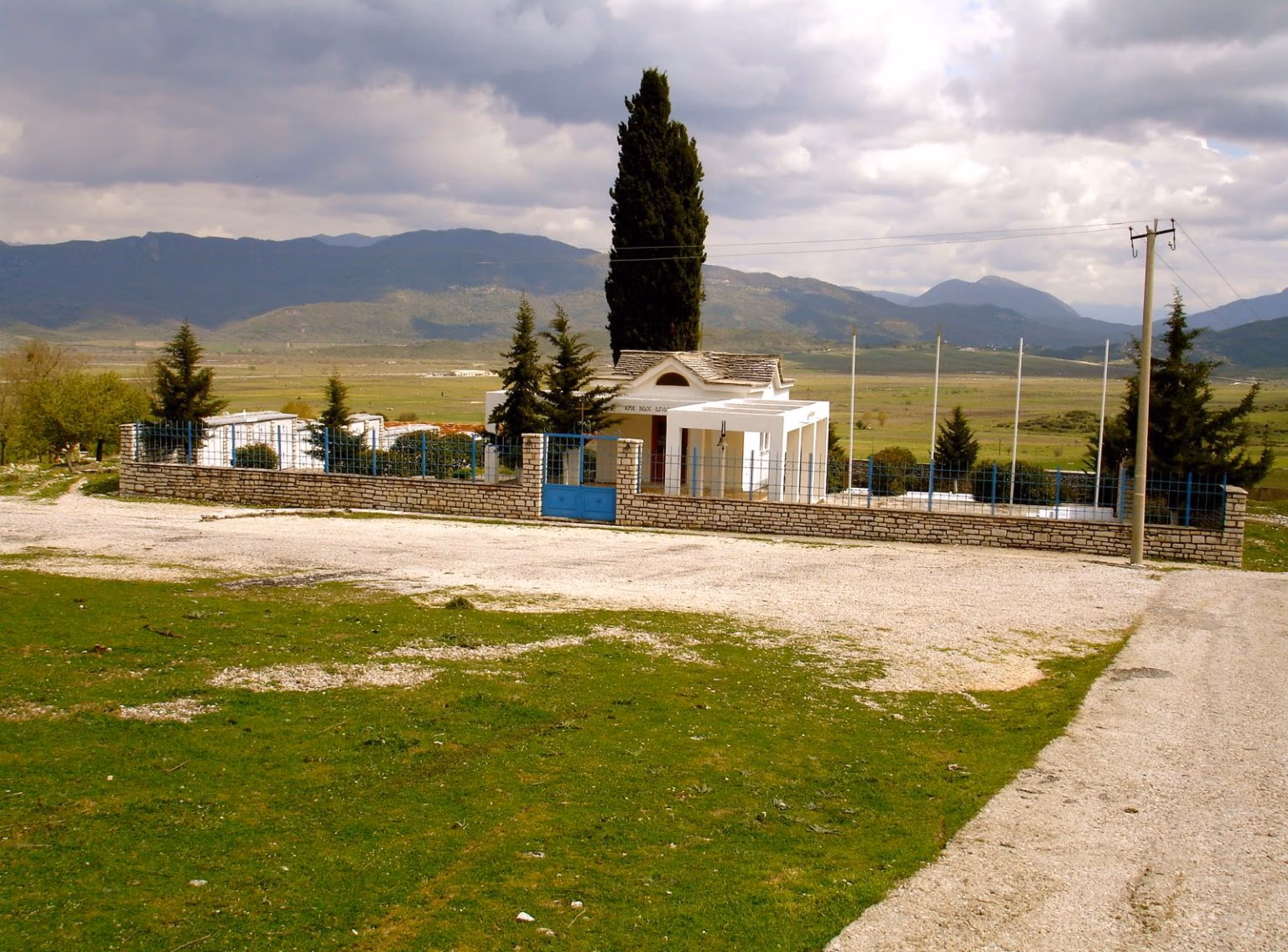 Small whitewashed chapel and grave rows on a grassy slope with mountains behind